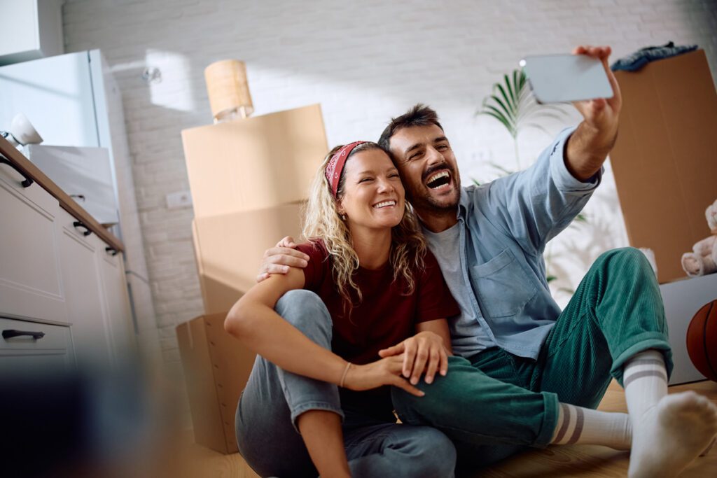 A happy couple sits on the floor of their new home surrounded by boxes after a successful homebuyer engagement strategy powered by AI.